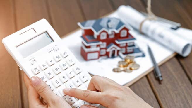 Una mano femenina operando una calculadora frente a un modelo de casa Villa
