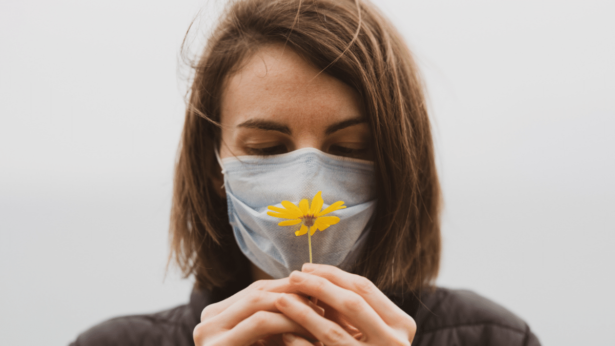 Mujer con una flores y mascarilla porque tiene alergia al polen y tiene síntomas