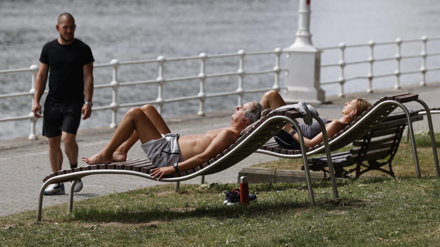 Dos personas toman el sol junto a la ría de Bilbao en mayo.