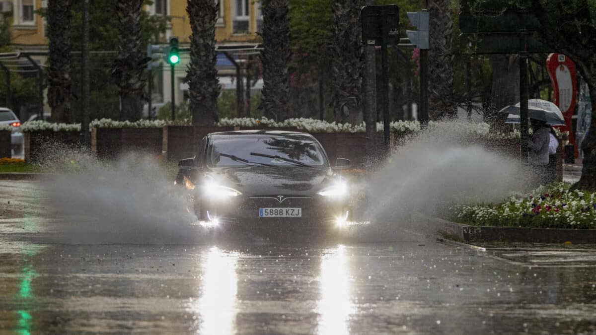 Un coche levanta el agua de la lluvia caída en la tarde
