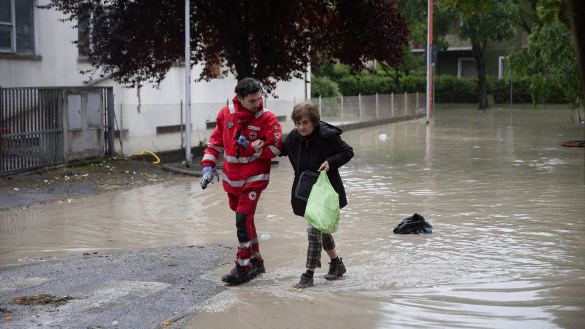 Un voluntario ayudando a una anciana por las fuertes inundaciones en Italia.
