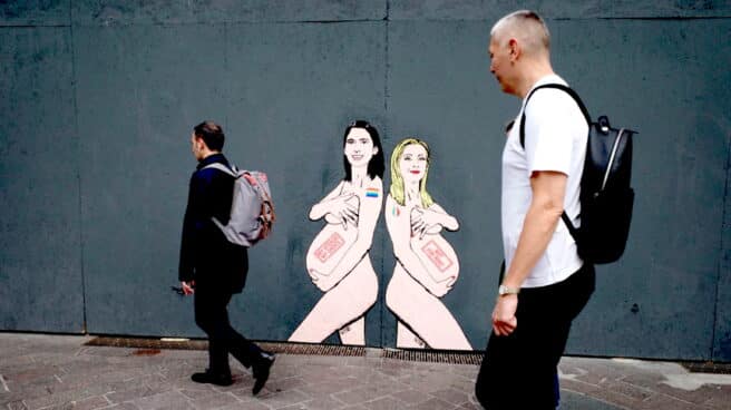 La gente camina junto a un mural de la primera ministra italiana Giorgia Meloni (R) y la líder del PD Elly Schlein, retratada por el artista 'aleXsandro Palombo' en Milán, Italia