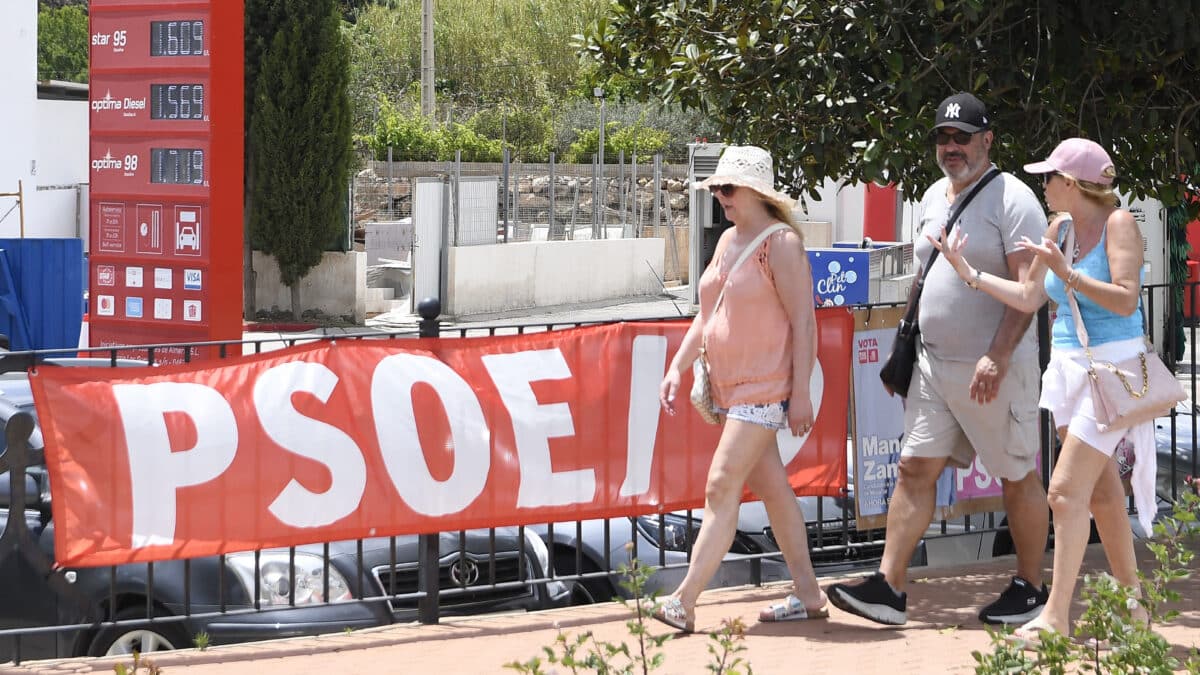 Unas personas caminan junto a una pancarta del PSOE de Mojácar (Almería) donde la dirección socialista ha suspendido cautelarmente de militancia