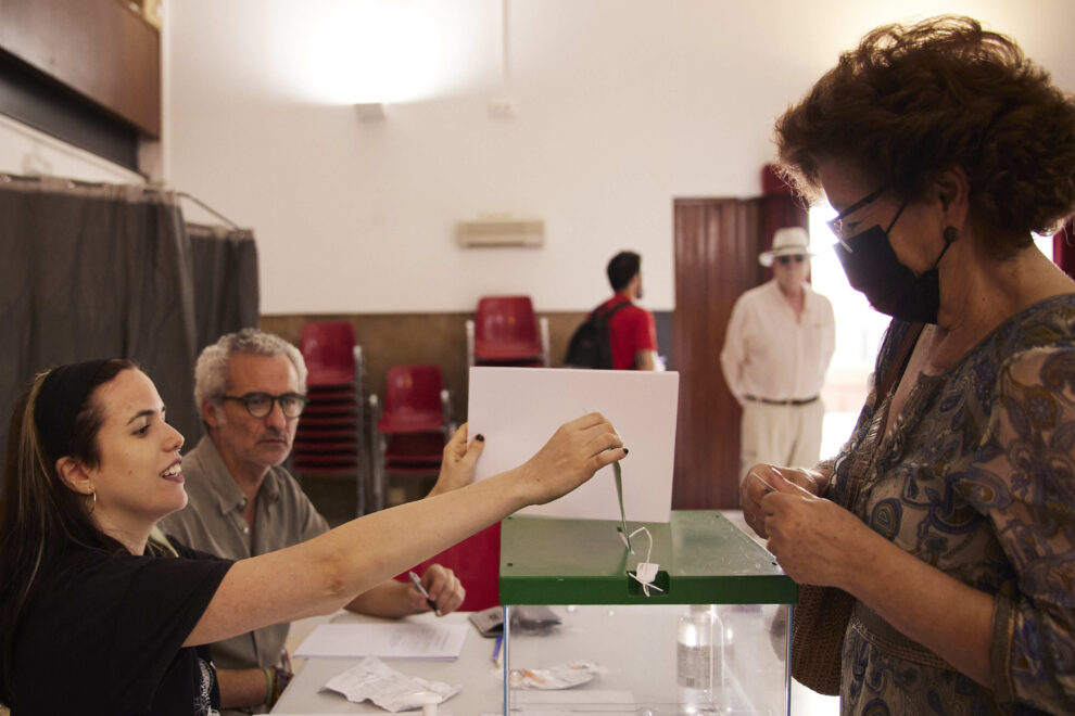 Mesa electoral en el que una mujer acude a votar y la presidenta de la mesa recoge su voto en un colegio electoral de España.