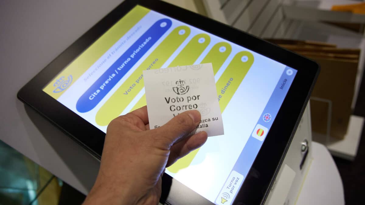 Una persona con un ticket de voto por correo en la oficina de Correos de Cibeles