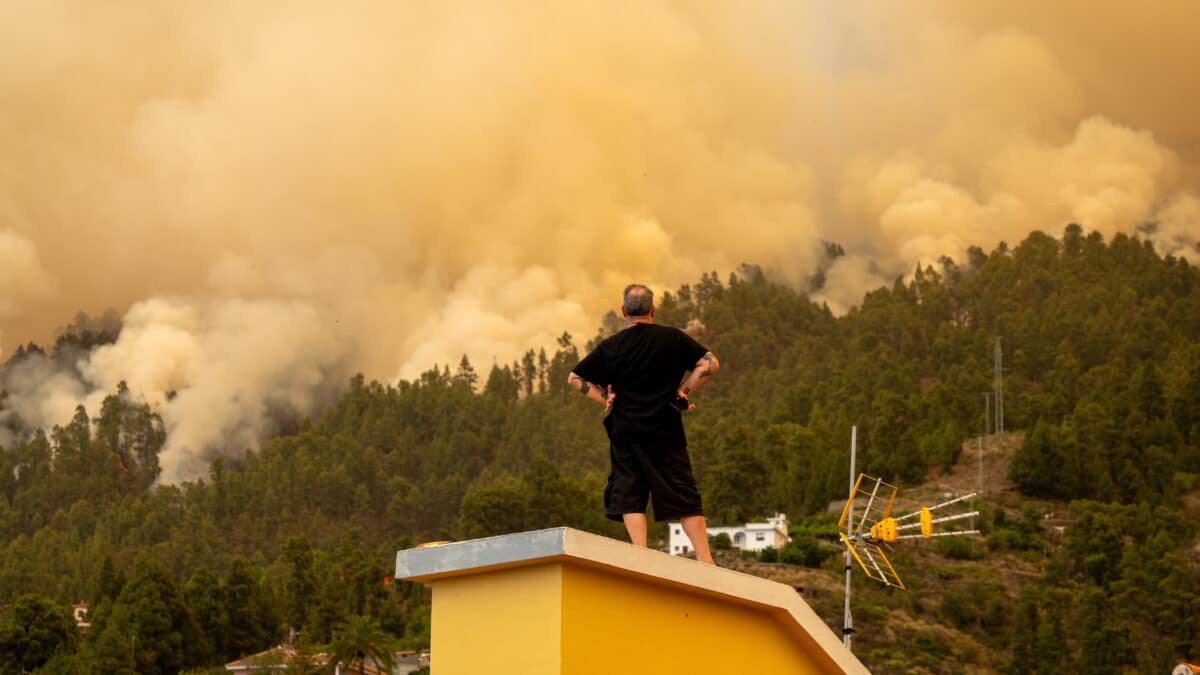 Un vecino observa desde el tejado de una casa el incendio forestal declarado en La Palma