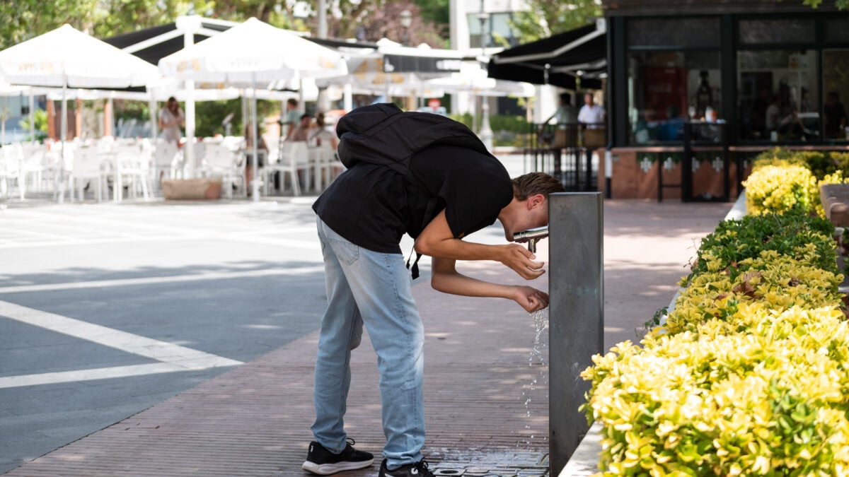 Un joven bebe agua de una fuente durante la cuarta ola de calor del verano