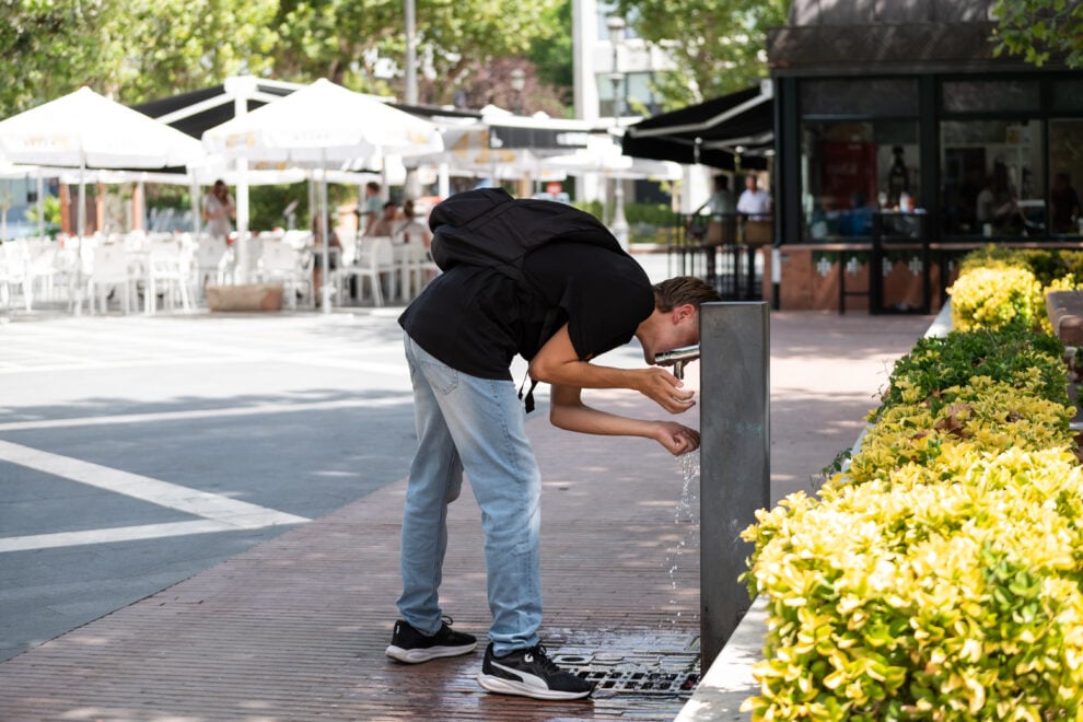 Un joven bebe agua de una fuente durante la cuarta ola de calor del verano,