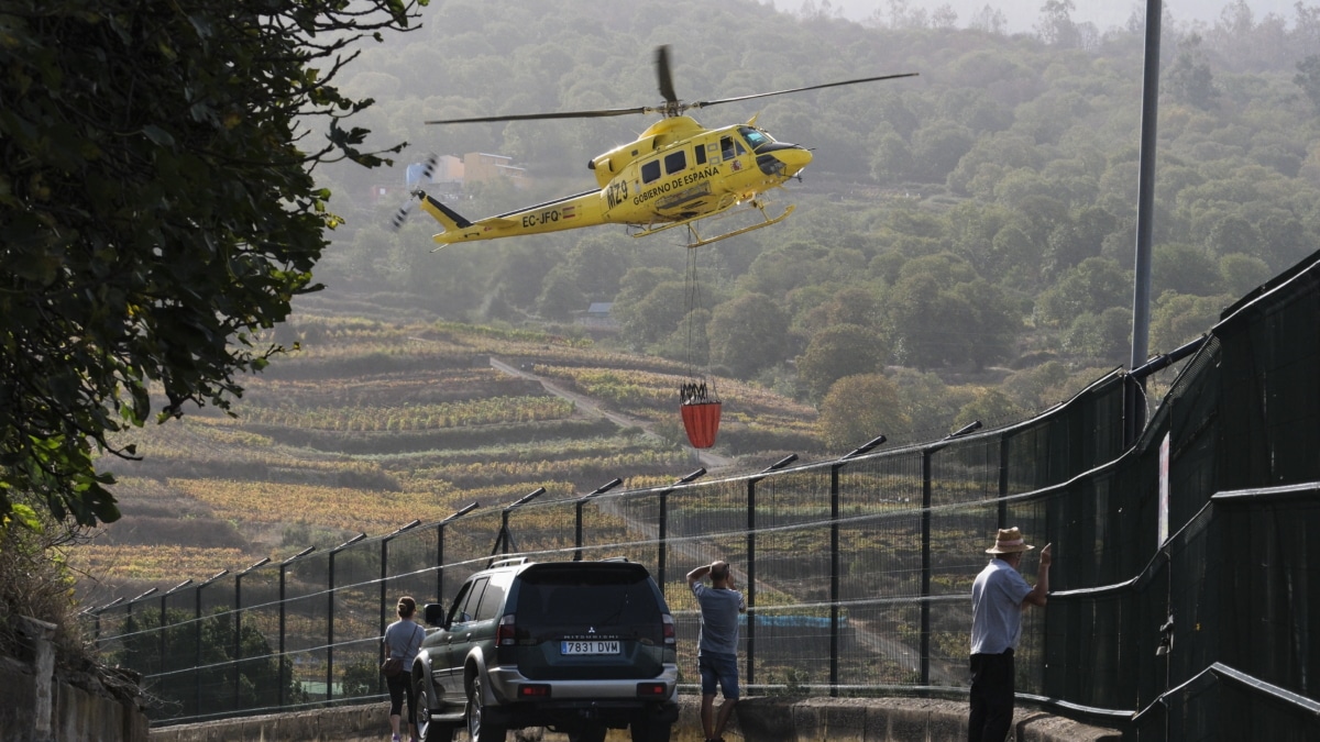 Varios vecinos de El Sauzal observan como un helicóptero que trabaja en las labores de extinción del incendio forestal de Tenerife, carga agua.