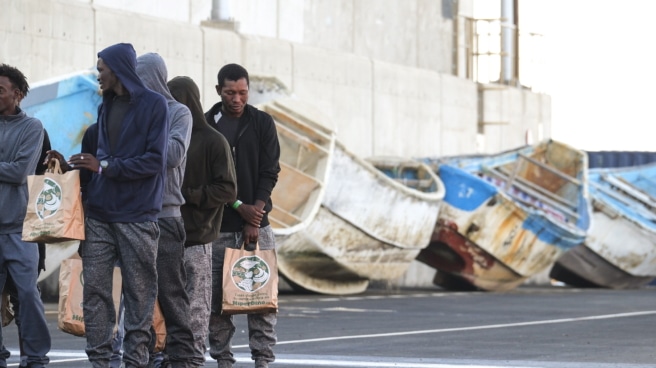 imagen de personas migrantes llegadas este lunes al puerto de Arinaga (Gran Canaria) con unos cayucos de fondo (Efe).