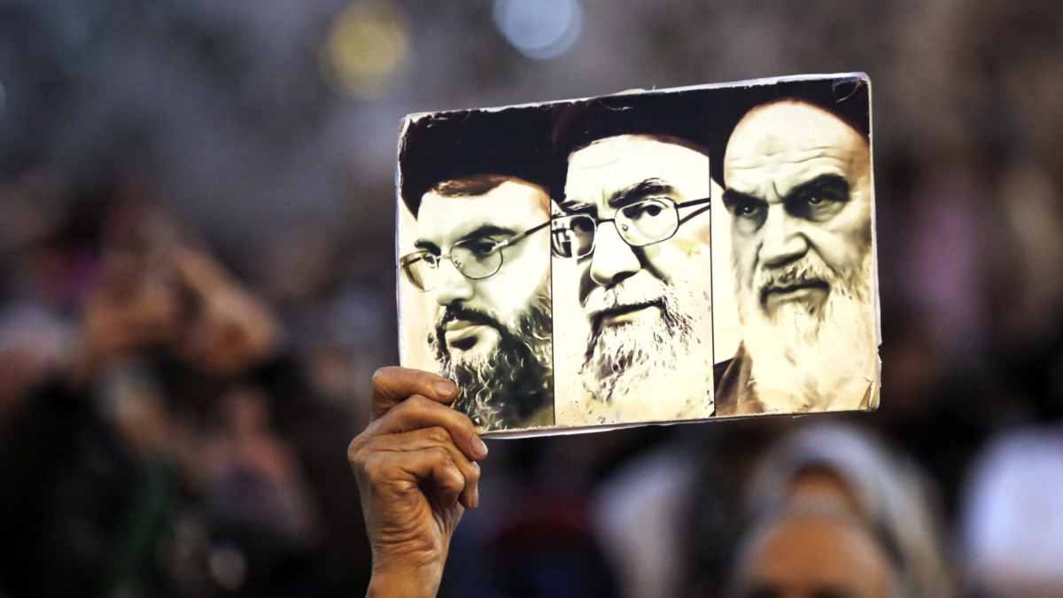 Un manifestante sostiene un cartel con los rostros de Nasralá, Jamenei y Jomeini en Beirut.