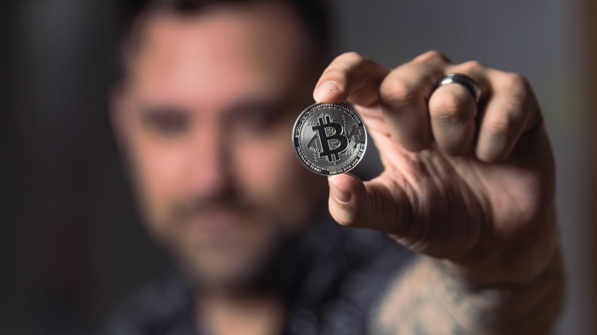 Un hombre sostiene una moneda de Bitcoin.