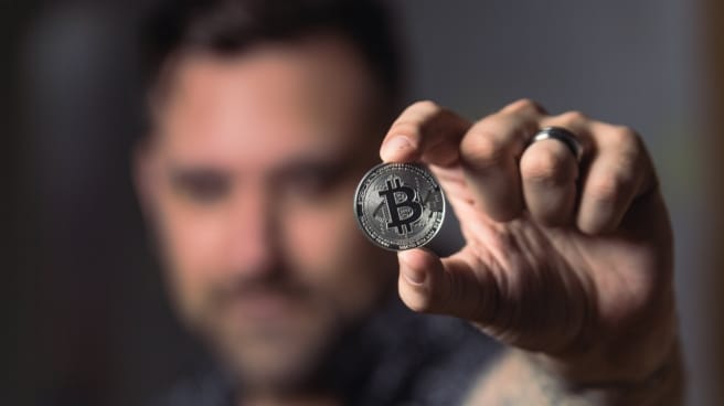 criptomonedas inversión Un hombre sostiene una moneda de Bitcoin.