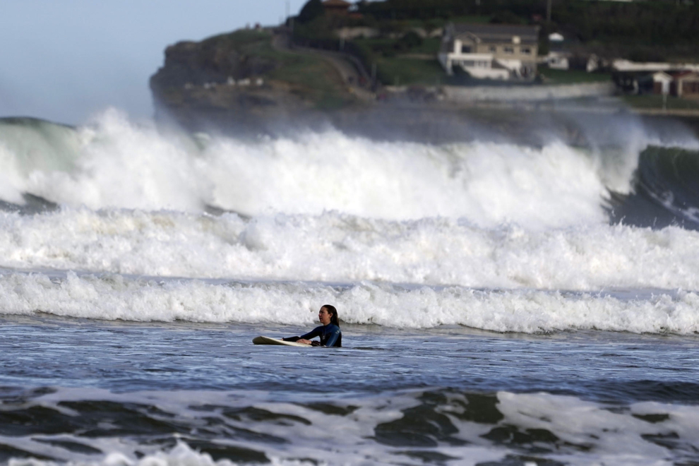 Una surfista con fuerte oleaje al fondo en la Playa de San Lorenzo este lunes, 1 de enero.