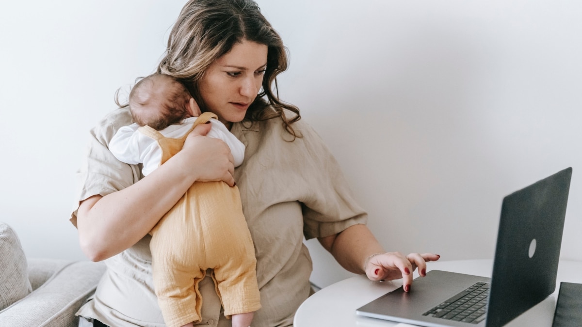 Una mujer sostiene a su bebé mientras trabaja delante del ordenador.