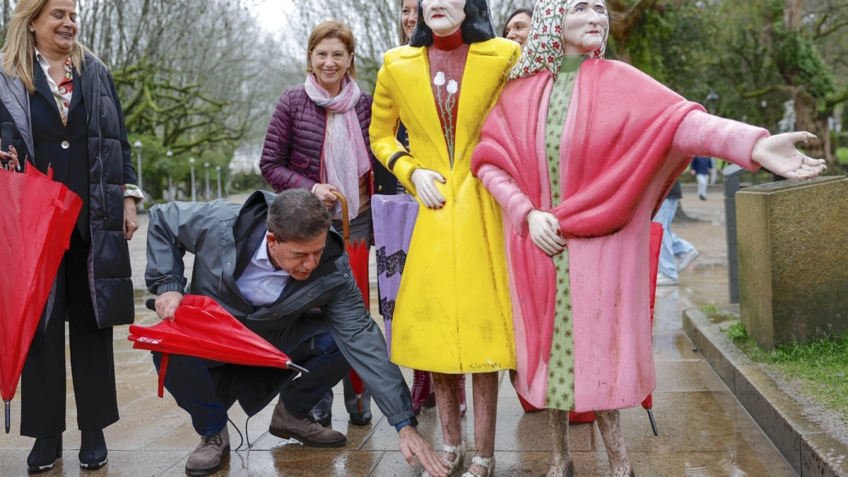 El candidato del PSOE, Xosé Ramón Besteiro (2i), limpia los zapatos de las escultura de "Las dos Marías", dentro de un paseo electoral este jueves en la Alameda de Santiago de Compostela.