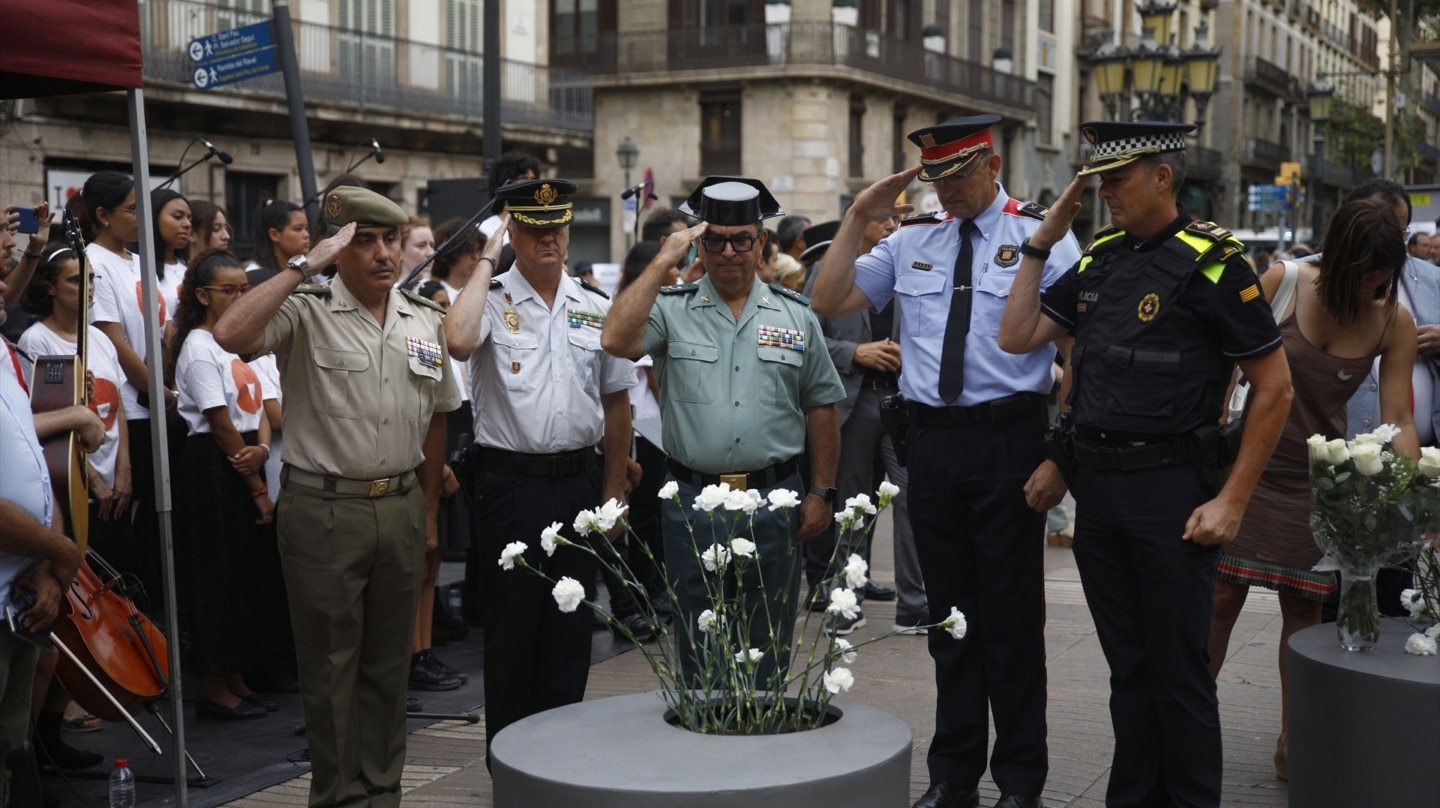 Representantes de los cuerpos policiales y el ejército se cuadran frente al monumento de las víctimas durante el homenaje a las víctimas del atentado en La Rambla.