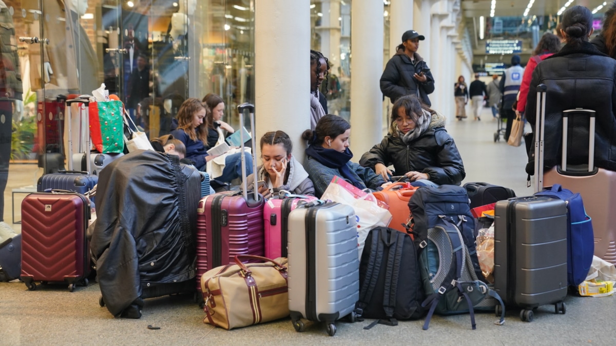 Unas chicas jóvenes esperan con maletas en una estación de Londres.