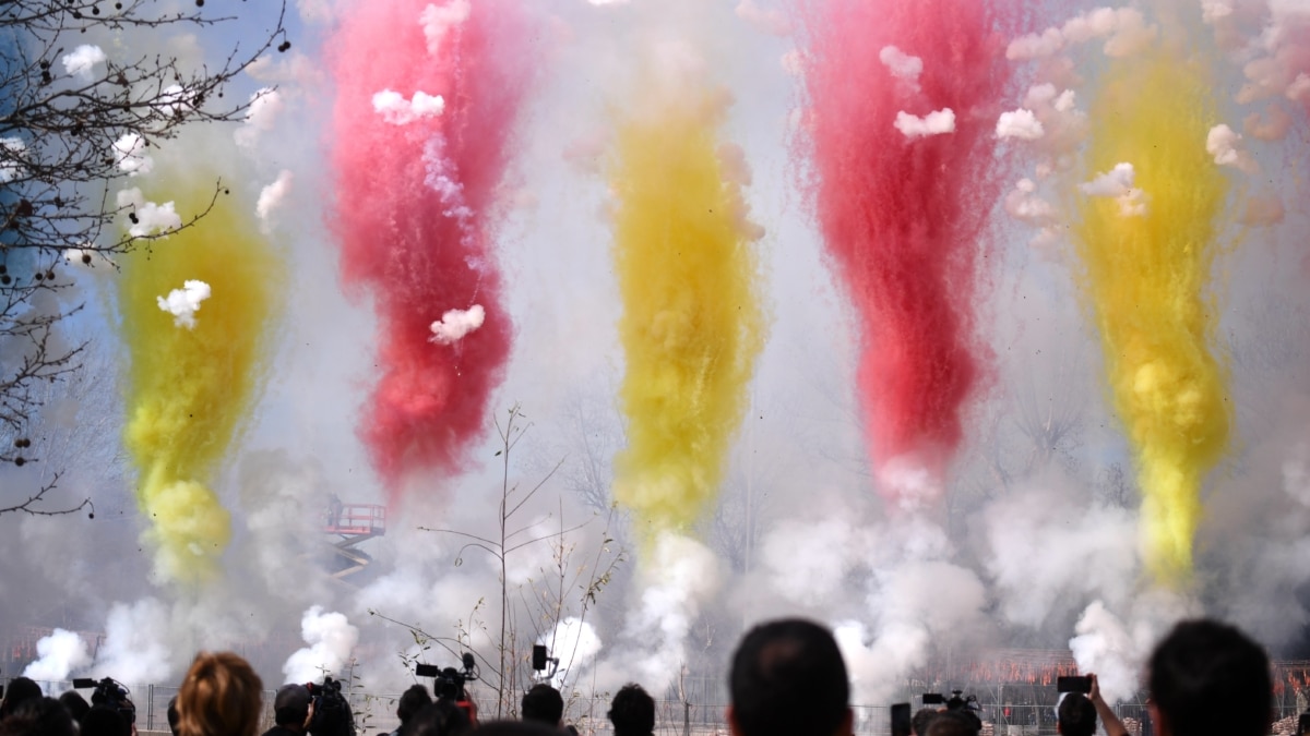 Varias personas observan el humo de colores durante la primera mascletà madrileña, en el Puente del Rey de Madrid Río