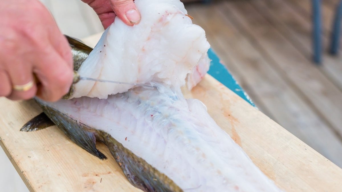 Una persona limpia un filete de Bacalao.