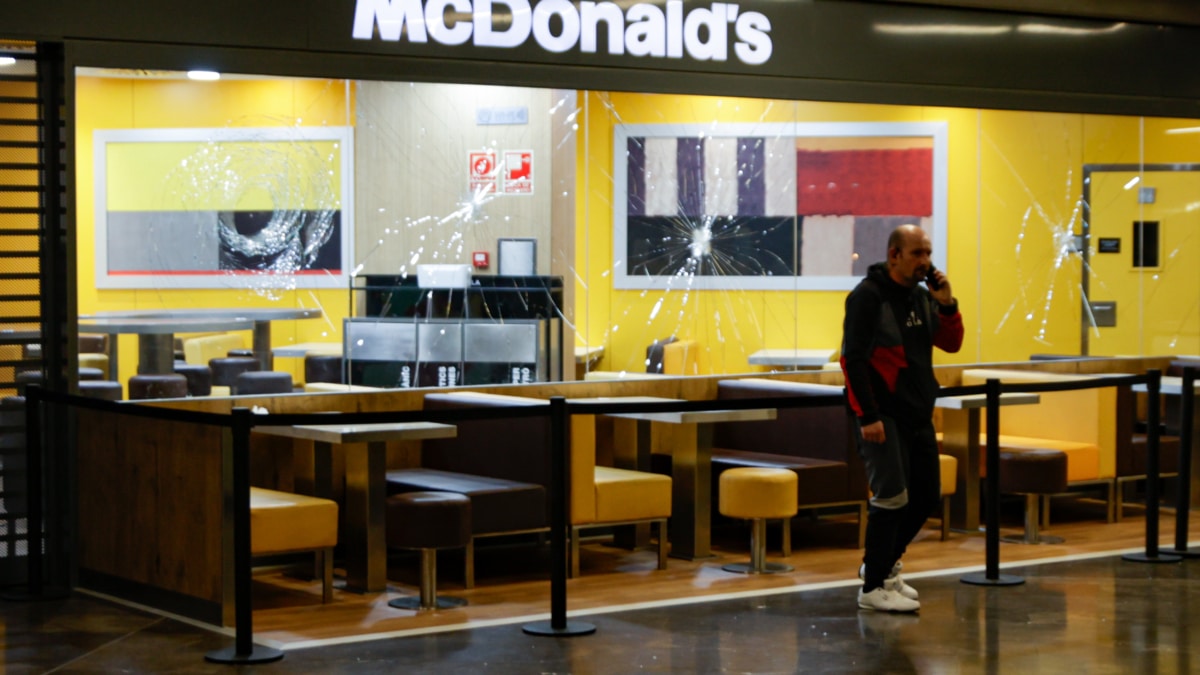 Una persona pasa delante del escaparate del McDonald's con los cristales rotos en el centro comercial Màgic Badalona