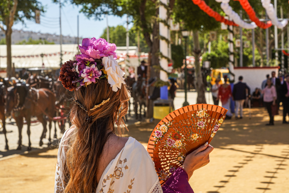 Una mujer vestida de flamenca se abanica en el recinto ferial de la Feria de Abril de Sevilla en el día más caluroso del año a 26 de abril del 2023.