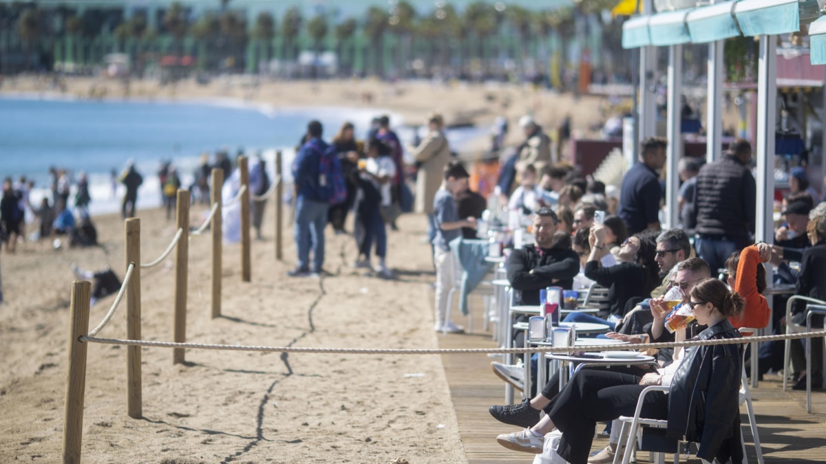 Miles de turistas disfrutan cerca de una playa en Barcelona, este lunes, a pesar del pronóstico de temporal de lluvias