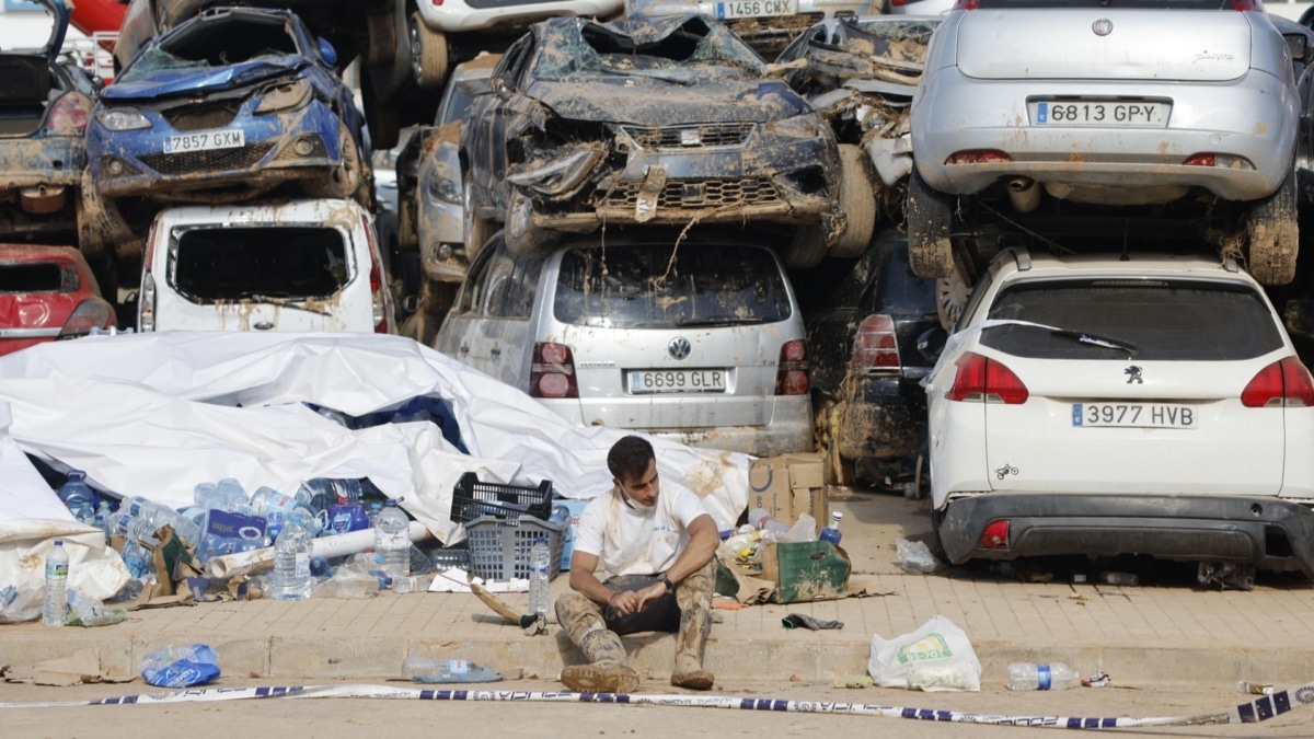Un voluntario descansa junto a una pila de vehículos destrozados en la riada en Masanasa (Valencia), este jueves.