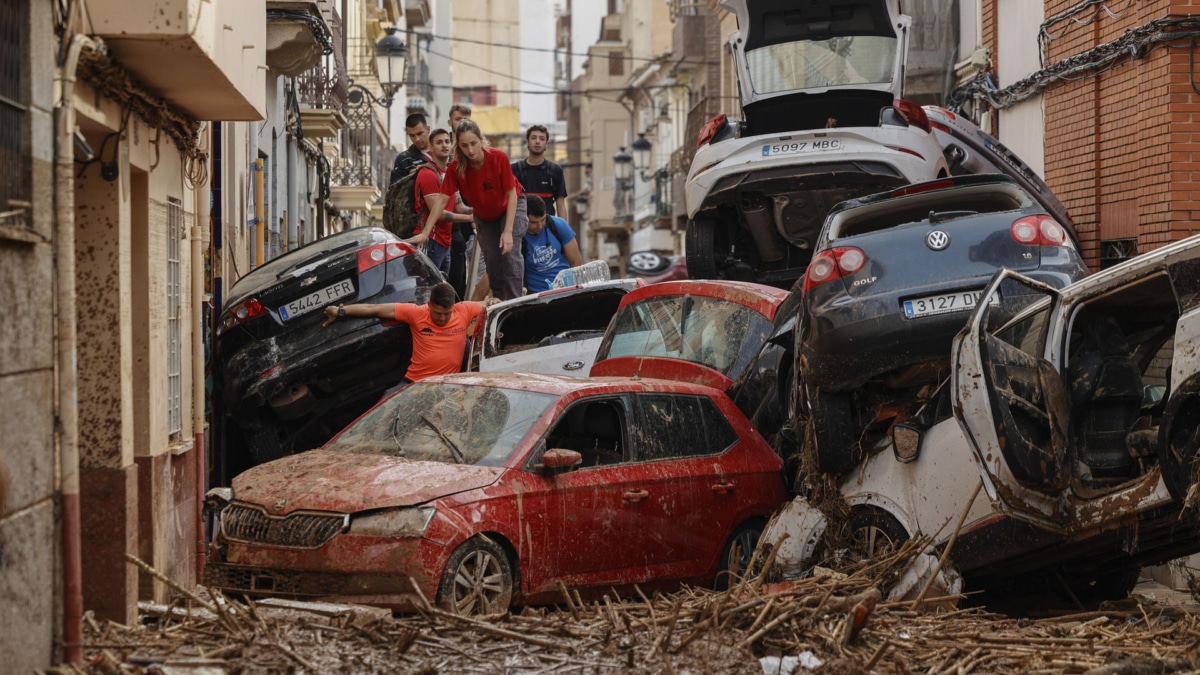 Vecinos de Paiporta pasan entre los coches amontonados por el temporal.