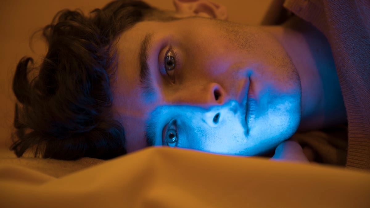 Joven acostado en la cama con poca iluminación.