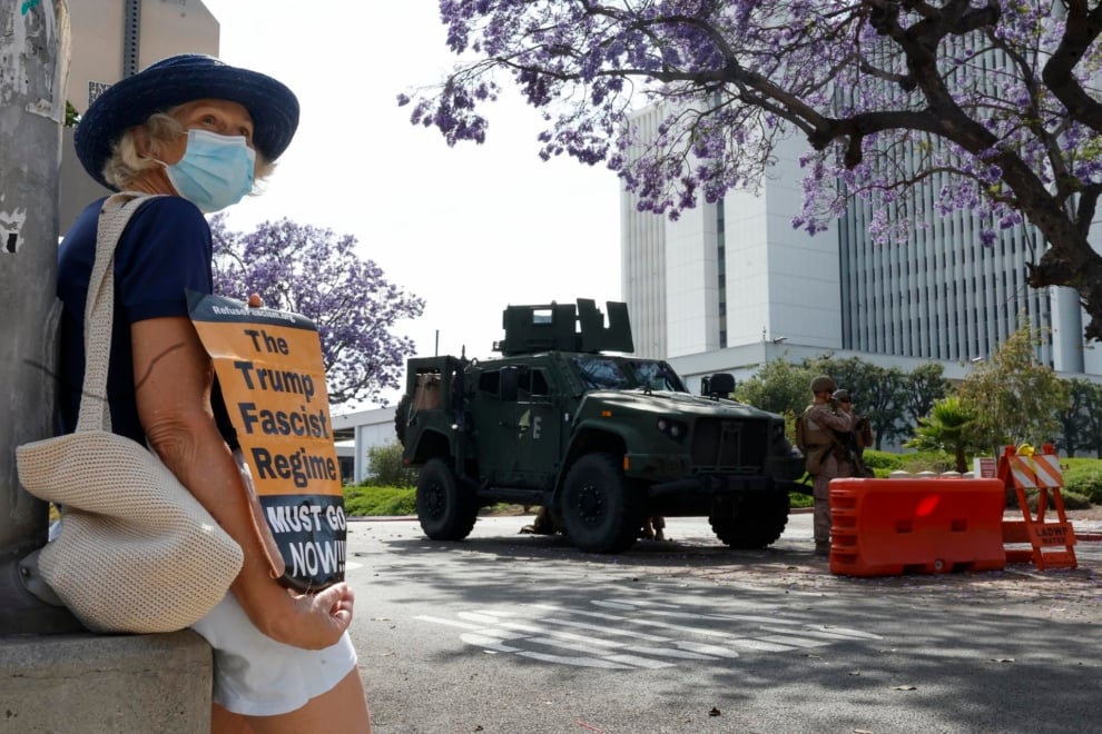 Una manifestante sostiene una pancarta mientras los marines protegen un edificio federal en Los Ángeles, en California. EFE/EPA/CAROLINE BREHMAN
