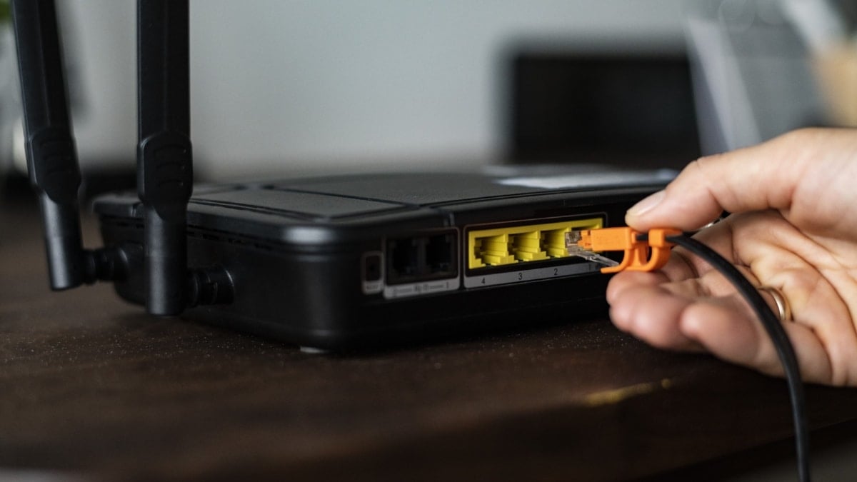 Hombre conectando un cable ethernet a un enrutador inalámbrico