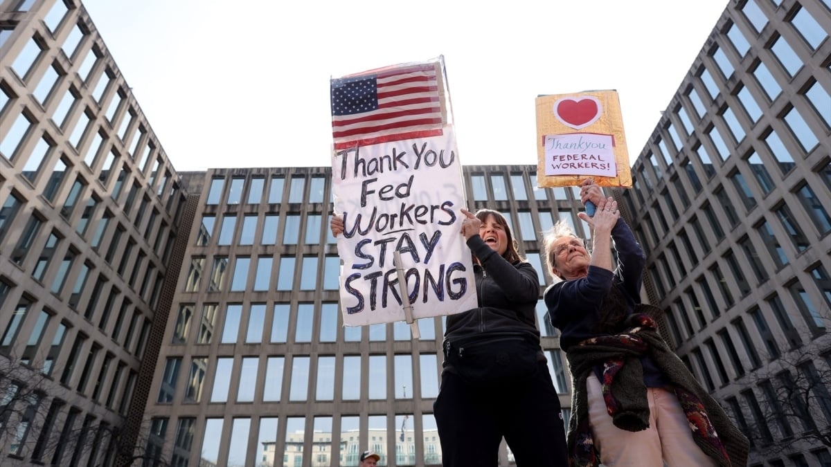 Dos mujeres muestransu apoyo a empleados públicos despedidos en Washington. En la pancarta más grande se lee "gracias, funcionarios, permaneced fuertes".