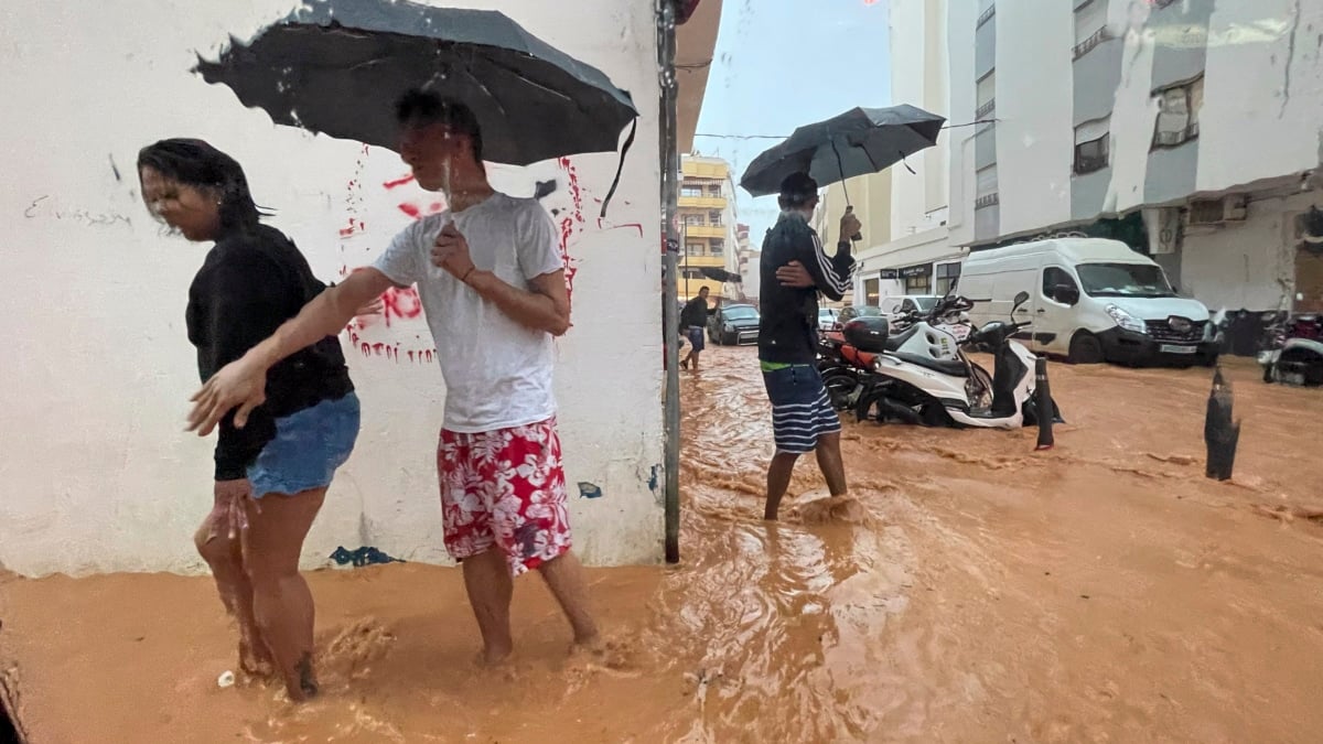 Personas caminan por calles anegadas en Ibiza debido a las intensas lluvias caídas este martes.