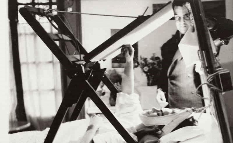 Frida pintando en su cama con Miguel Covarrubias a su lado.