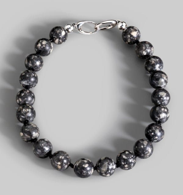 Pulsera creada con 20 cuentas esféricas talladas a partir del meteorito lunar NWA 12691, recuperado en 2017 en el corredor del Sáhara (Mauritania, frontera con Sáhara Occidental y Argelia). La Luna es uno de los materiales más escasos en la Tierra: se estima que existe menos de 2.500 kg en total y gran parte está en museos o colecciones institucionales; los meteoritos lunares disponibles para coleccionistas son una fracción mínima. Las cuentas de esta joya tan especial —de 8,2 mm y 3,66 ct cada una— proceden del mismo fragmento que originó varias esferas mayores, y fueron elaboradas por el artesano Martin Roberts siguiendo la tradición de The Sphere Maker's Craft. Como toda brecha feldespática lunar, contiene anortita blanca, olivino y piroxenos, minerales raros o inexistentes en la superficie terrestre. Una pieza literalmente hecha de la Luna, con una puja inicial de 45.00 dólares y que podría alcanzar los 90.000.