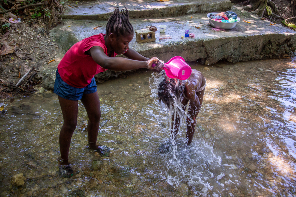 Una mujer ayuda a una niña a lavarse en un arroyo en Marouge, Haití.