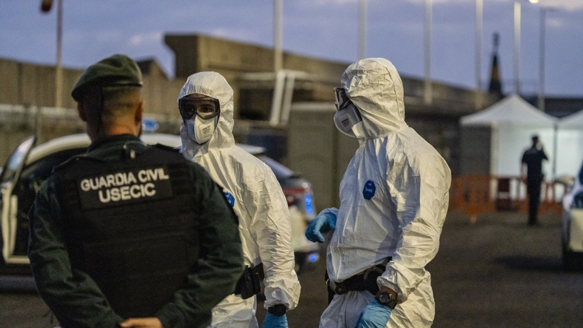 Personas con mono EPI esperan en el puerto mientras el crucero MV Hondius fondea cerca del puerto de Granadilla, este domingo