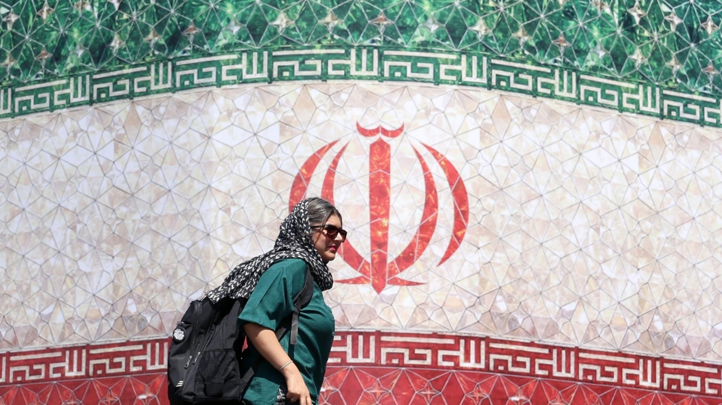 Una mujer iraní pasa junto a una valla publicitaria con la bandera nacional de Irán en la plaza Enqelab de Teherán, Irán, este domingo.