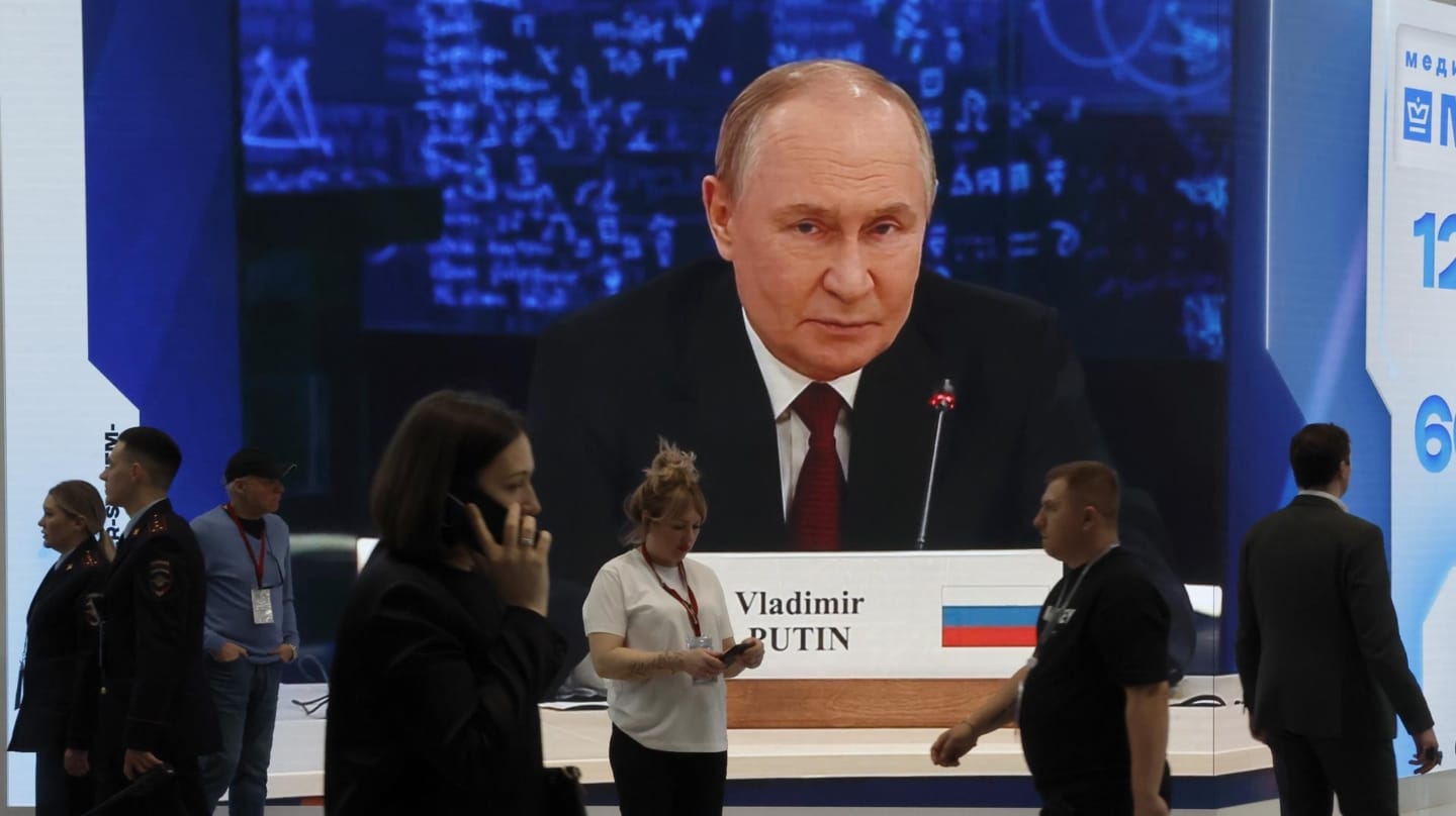 Los participantes en el Foro de San Petersburgo pasan delante de una pantalla con la imagen de Putin