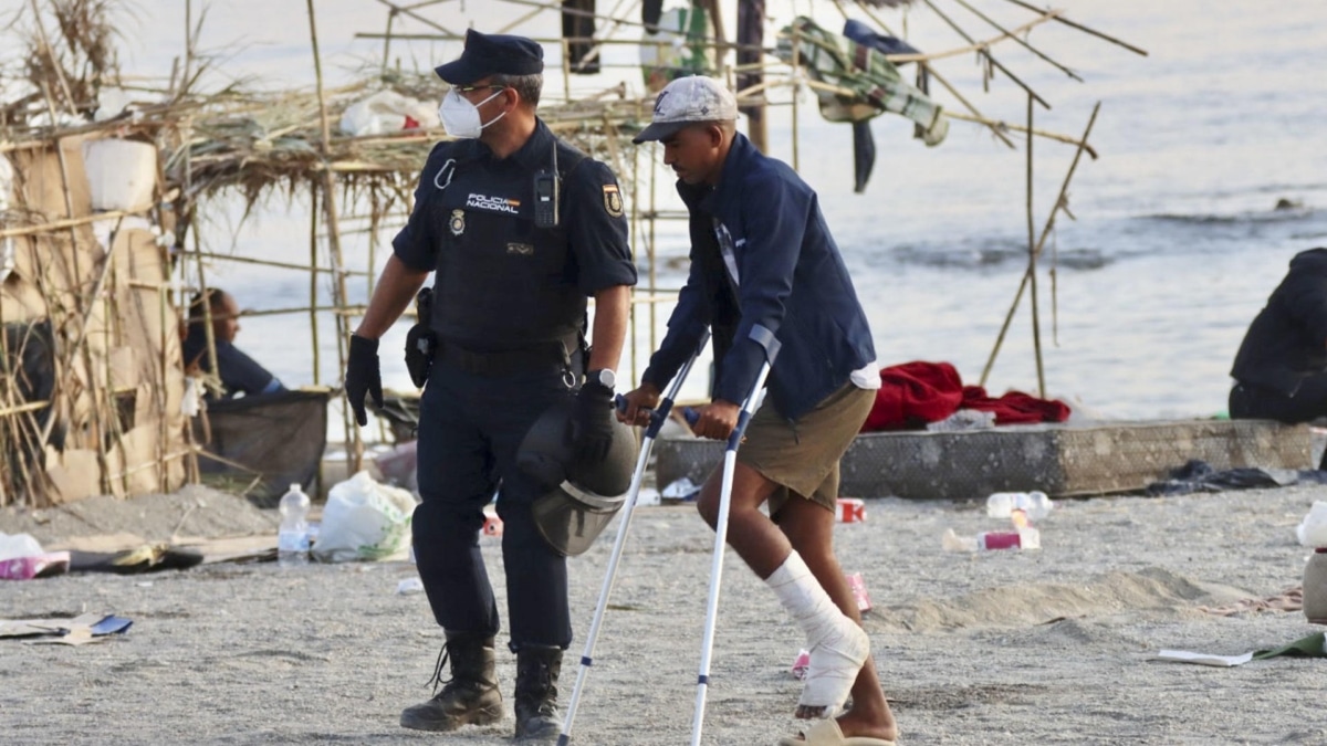 Un policía acompaña a uno de los migrantes durante el desalojo de la playa del Trampolín en Ceuta este jueves