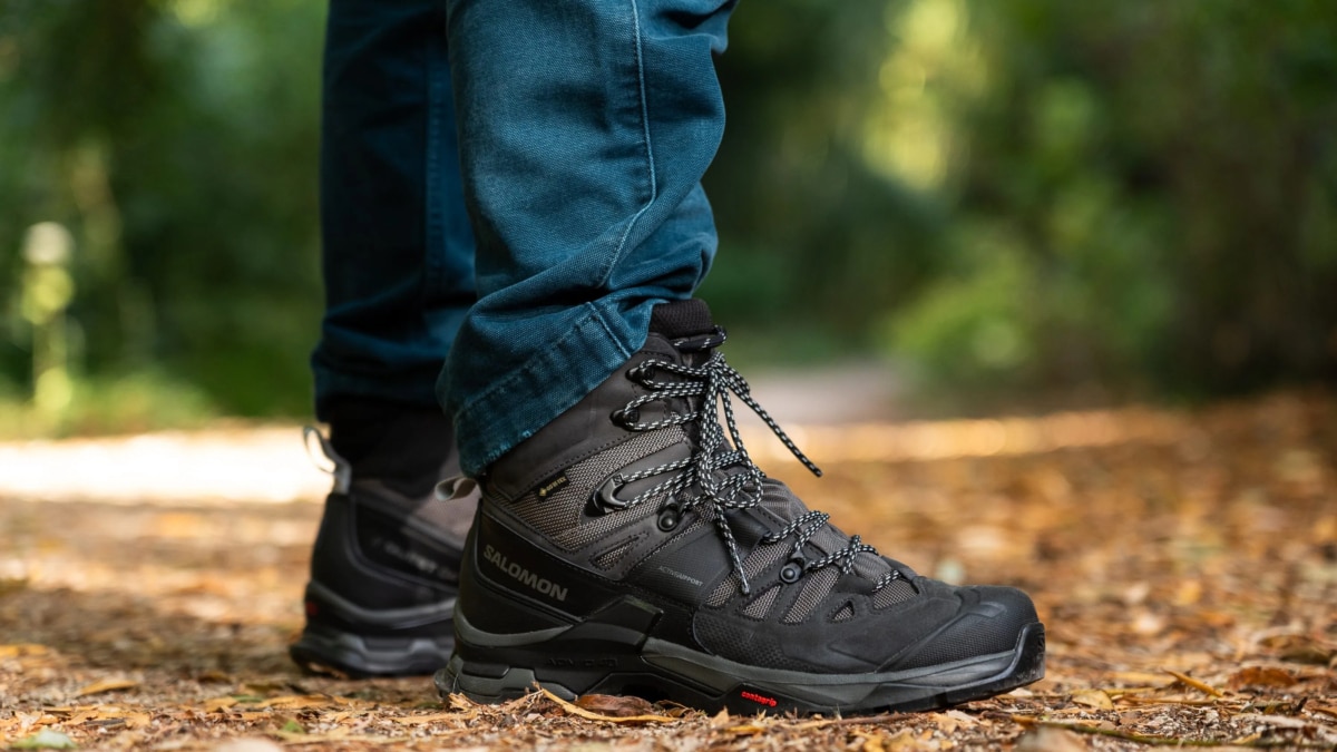 Botas de montaña Salomon negras con Gore-Tex puestas con un pantalón vaquero sobre un sendero de bosque cubierto de hojas secas