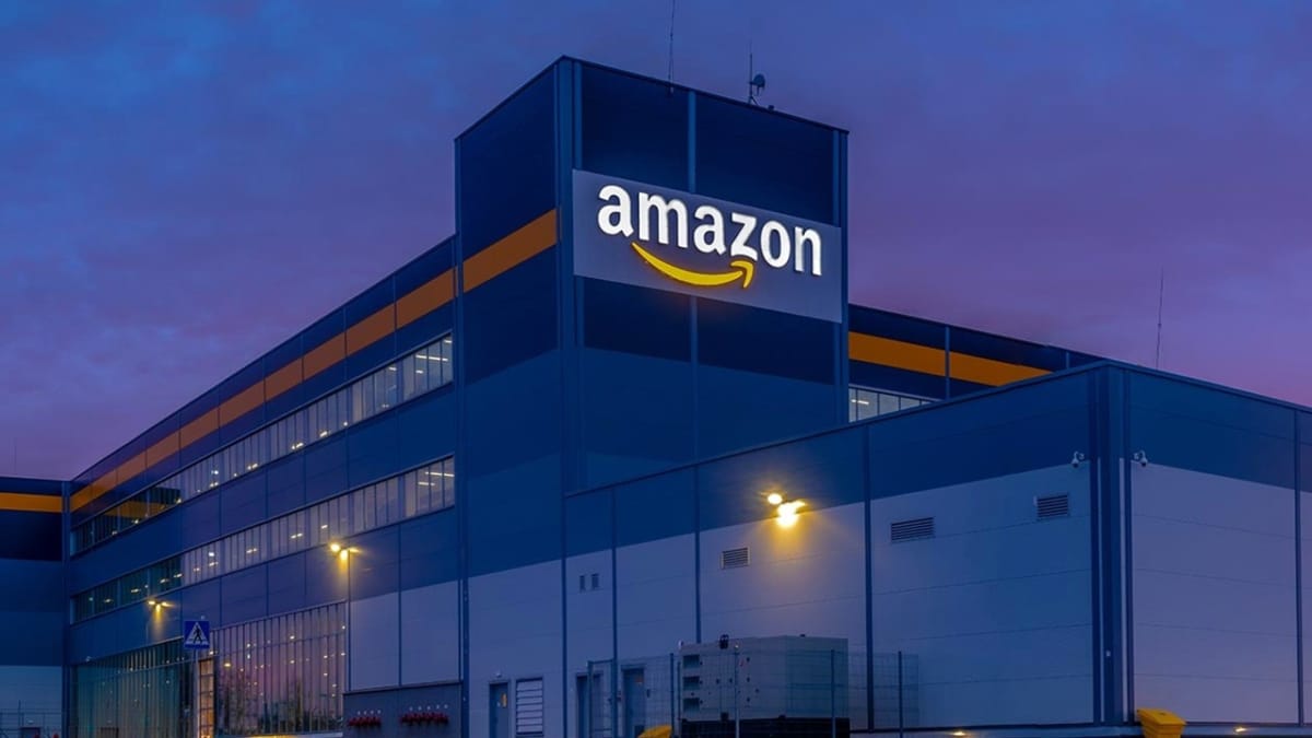 Fachada de un centro logístico de Amazon al anochecer, con el logotipo iluminado en lo alto del edificio